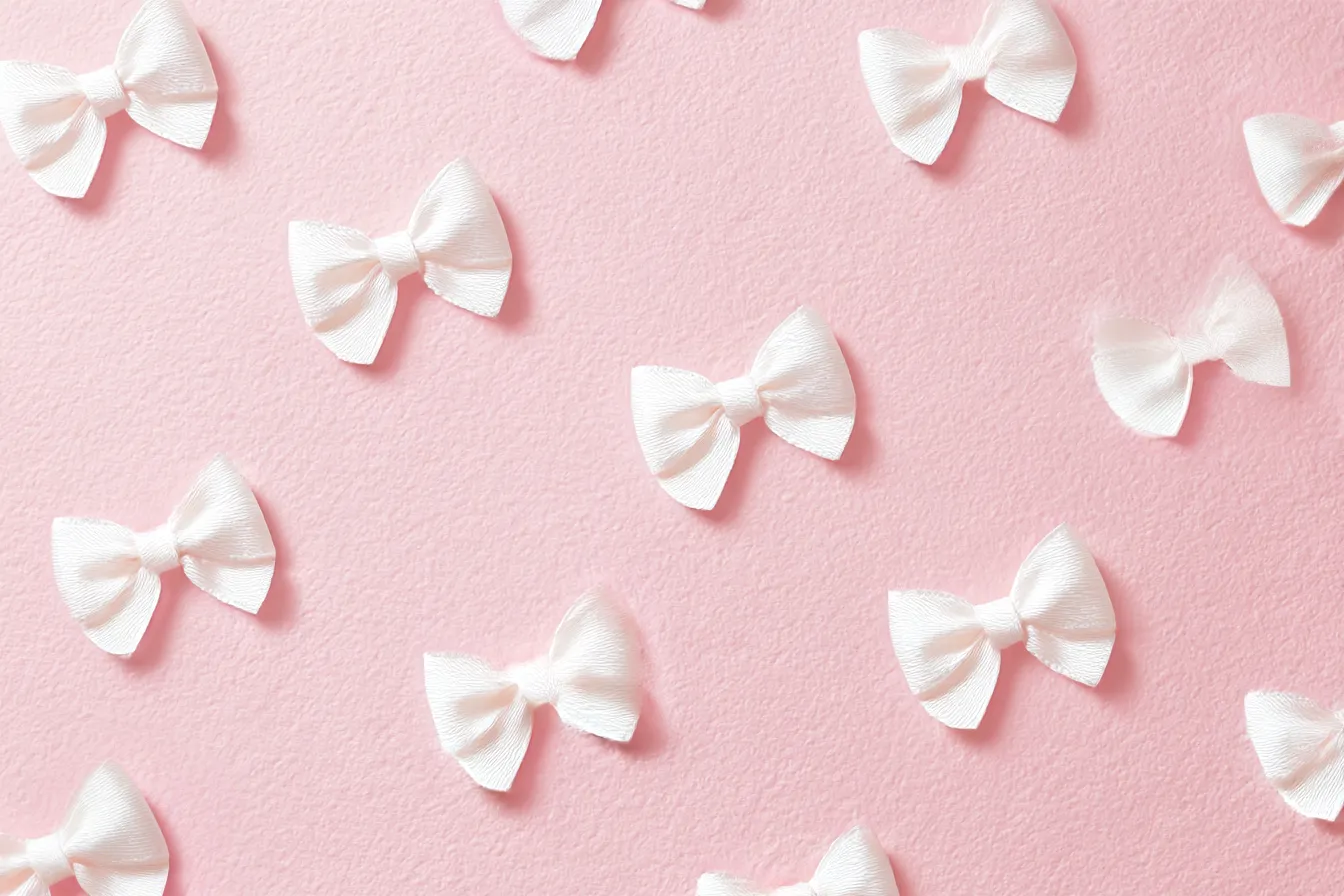リボン背景とホワイトサテン調|くすみピンクの背景に白いリボンが規則的に配置され、甘さと清楚さが際立つ構成。立体感のある素材表現がリアルで、ガーリーな世界観を上品に仕上げている。