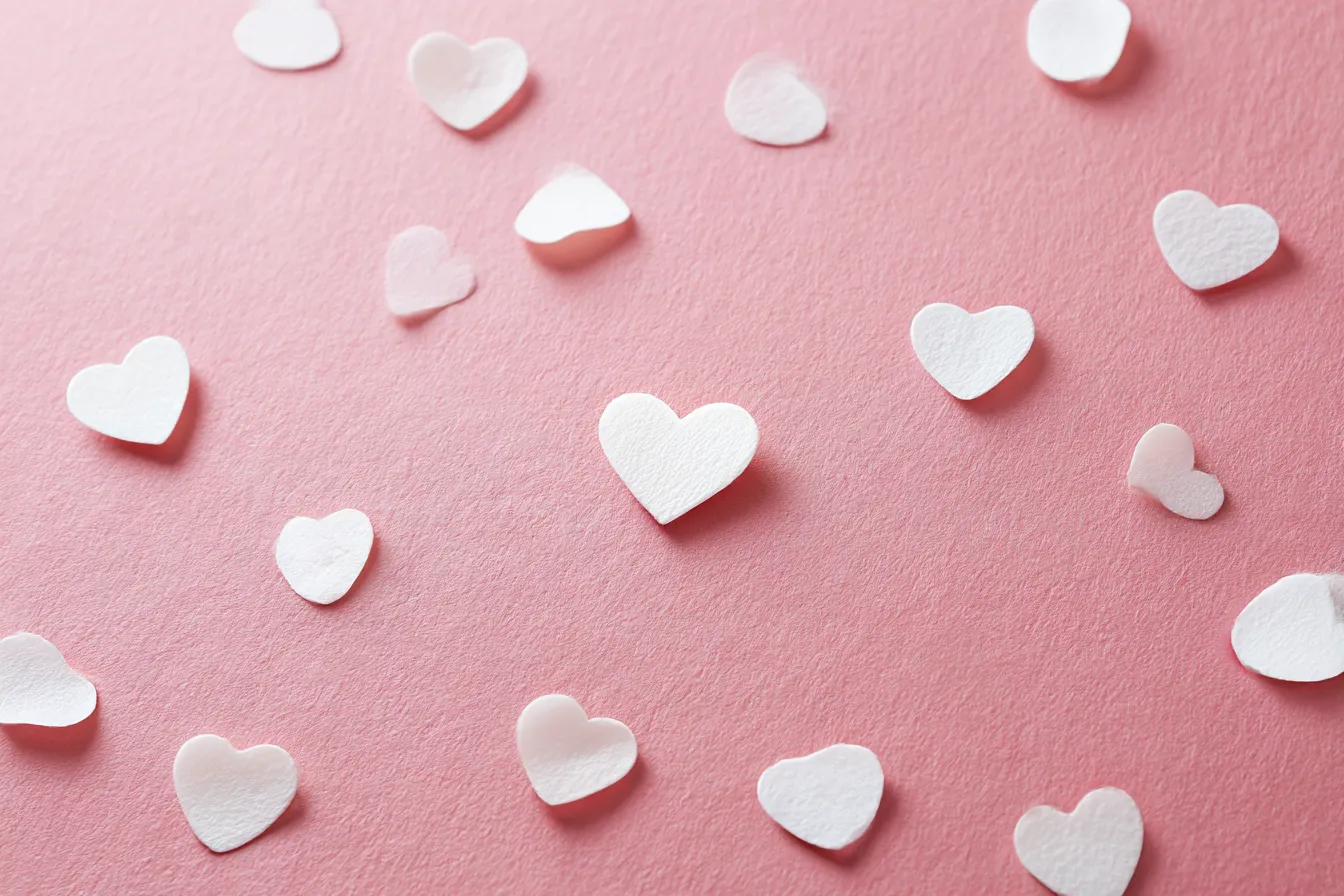 ハートと紙質ピンクの韓国背景|ざらっとした紙感のあるピンク背景に白いハートがふわりと配置されたデザイン。韓国っぽいやさしいガーリーテイストで、恋愛系や推し活イラストの背景にも最適です。