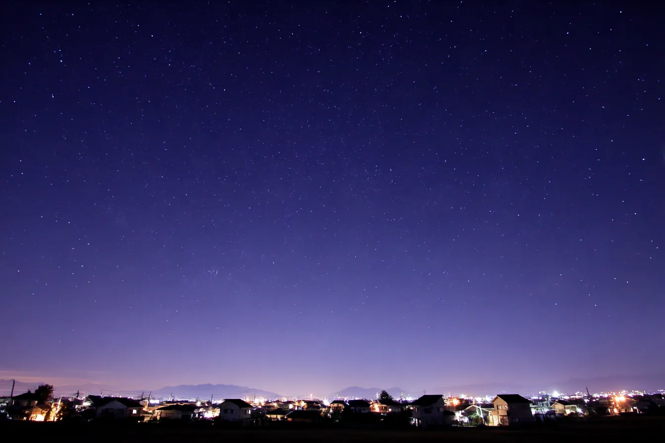 夜景背景×星空と郊外住宅｜星が広がる紺碧の空と郊外の家並みが織りなす優しい夜の風景。どこか懐かしく温かな空気感があり、日常系やノスタルジック演出に最適な背景です。