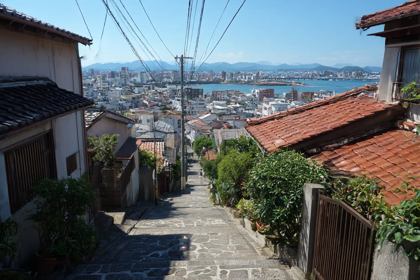 ジブリ背景　坂道から見下ろす港町｜石畳の坂と赤瓦の屋根が続く町並みと海の広がりが描かれたジブリ背景。生活感ある風景と空の奥行きが、懐かしい記憶を呼び起こす構図。