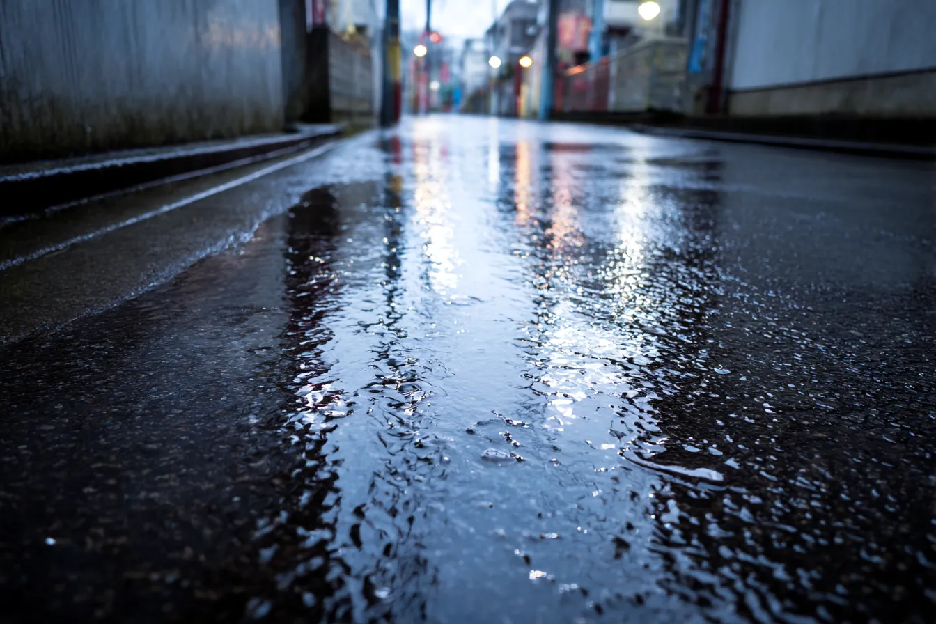 路地裏背景　雨上がりの濡れた舗道｜夕暮れの光が反射する濡れたアスファルトが印象的な路地裏背景。しっとりとした雰囲気と静けさが、ノスタルジックな情緒を醸し出す構図。