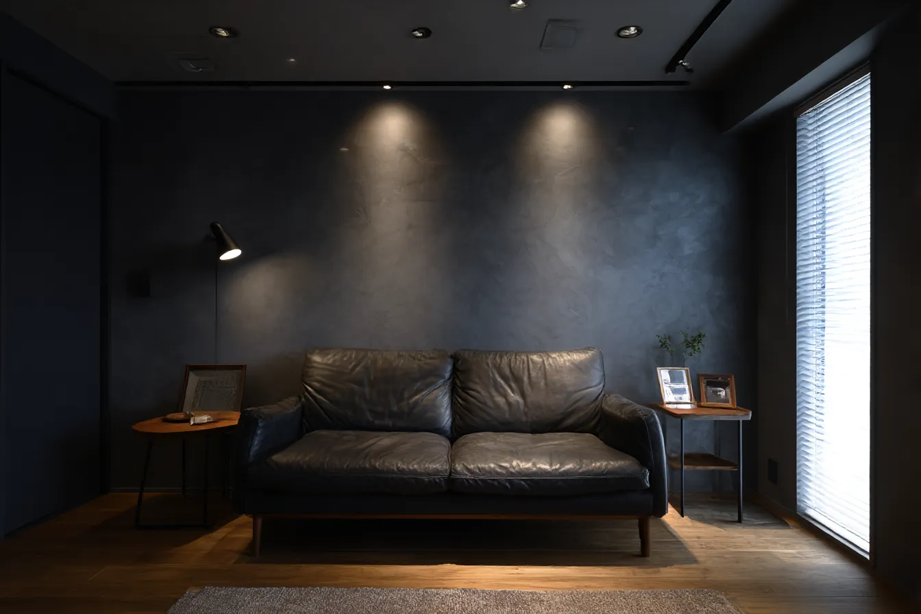 モノトーンソファの部屋背景｜暗めの照明と黒革ソファが特徴的な、シックで大人っぽい部屋背景。落ち着いた雰囲気や夜のリラックスシーン、ドラマチックな演出に適している。