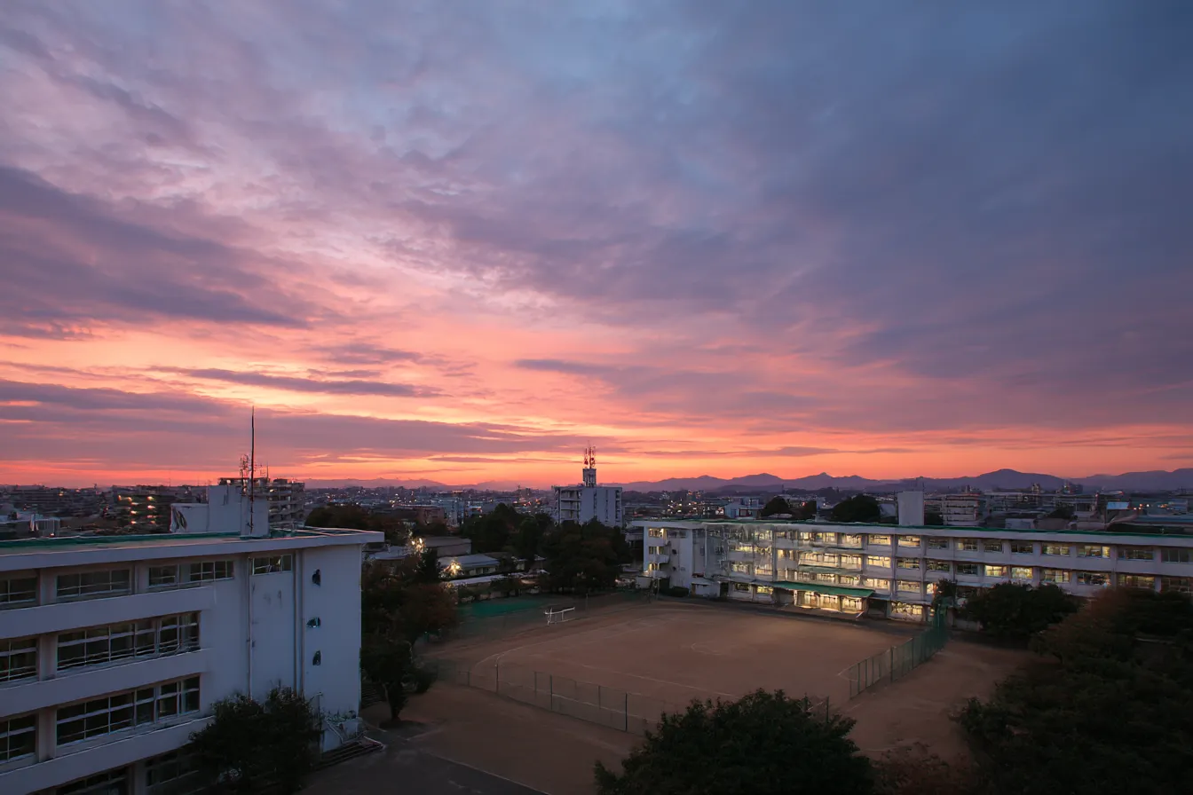 夕焼けと校舎の学校背景｜校舎全体が夕焼けに染まる情景が美しい学校背景。赤紫色の空が切なさと温もりを同時に伝え、感傷的なストーリーシーンに深みを与える。
