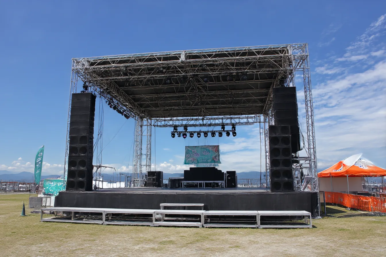 屋外フェス用ステージ背景｜青空の下に設営された金属フレームの屋外ステージ背景。音楽フェスや野外イベントに適した開放感とパワフルな印象を与える。