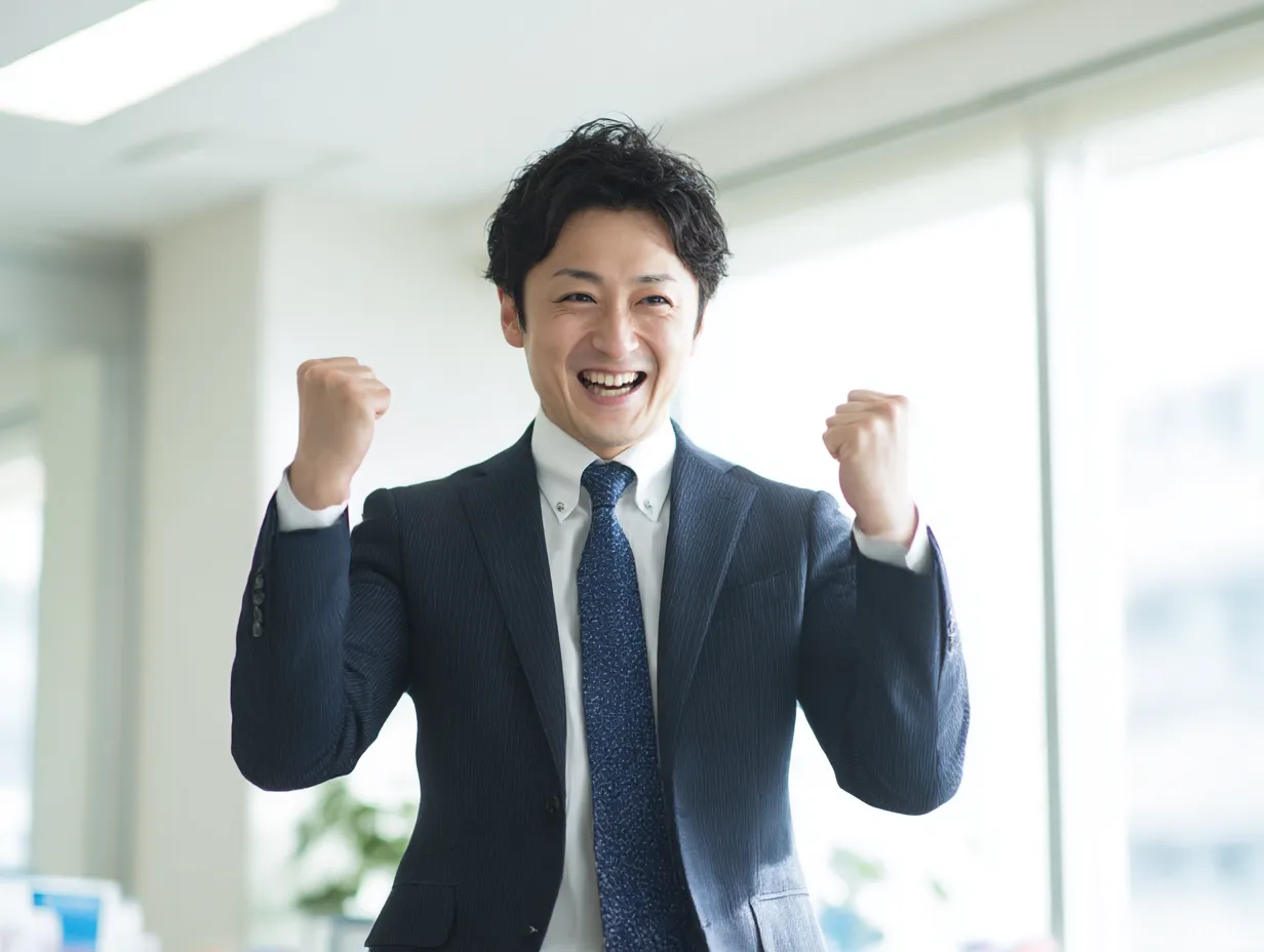 がんばれガッツポーズの男性２｜両手を高く挙げたガッツポーズで達成感を表現するビジネスパーソン。清潔感あるオフィスと明るい光が活気をプラス。がんばれの瞬間を切り取った写真として幅広く活用可能。