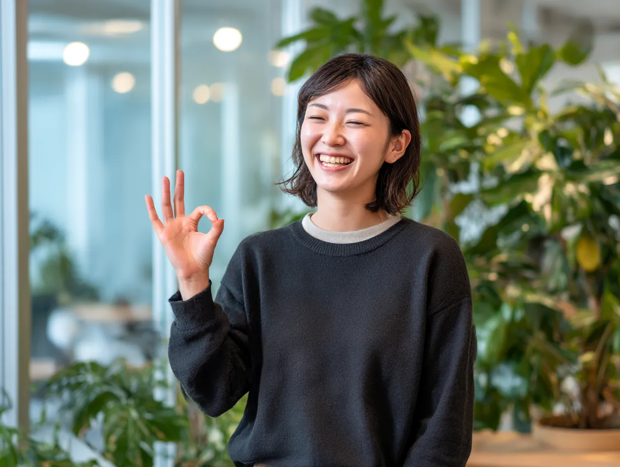 OKサインで笑顔のカジュアル感｜リラックスした服装と自然な笑顔が調和し、柔らかいグリーン背景と共にカジュアルなOKの雰囲気を表現。親しみやすさを重視したビジネス素材に最適です。