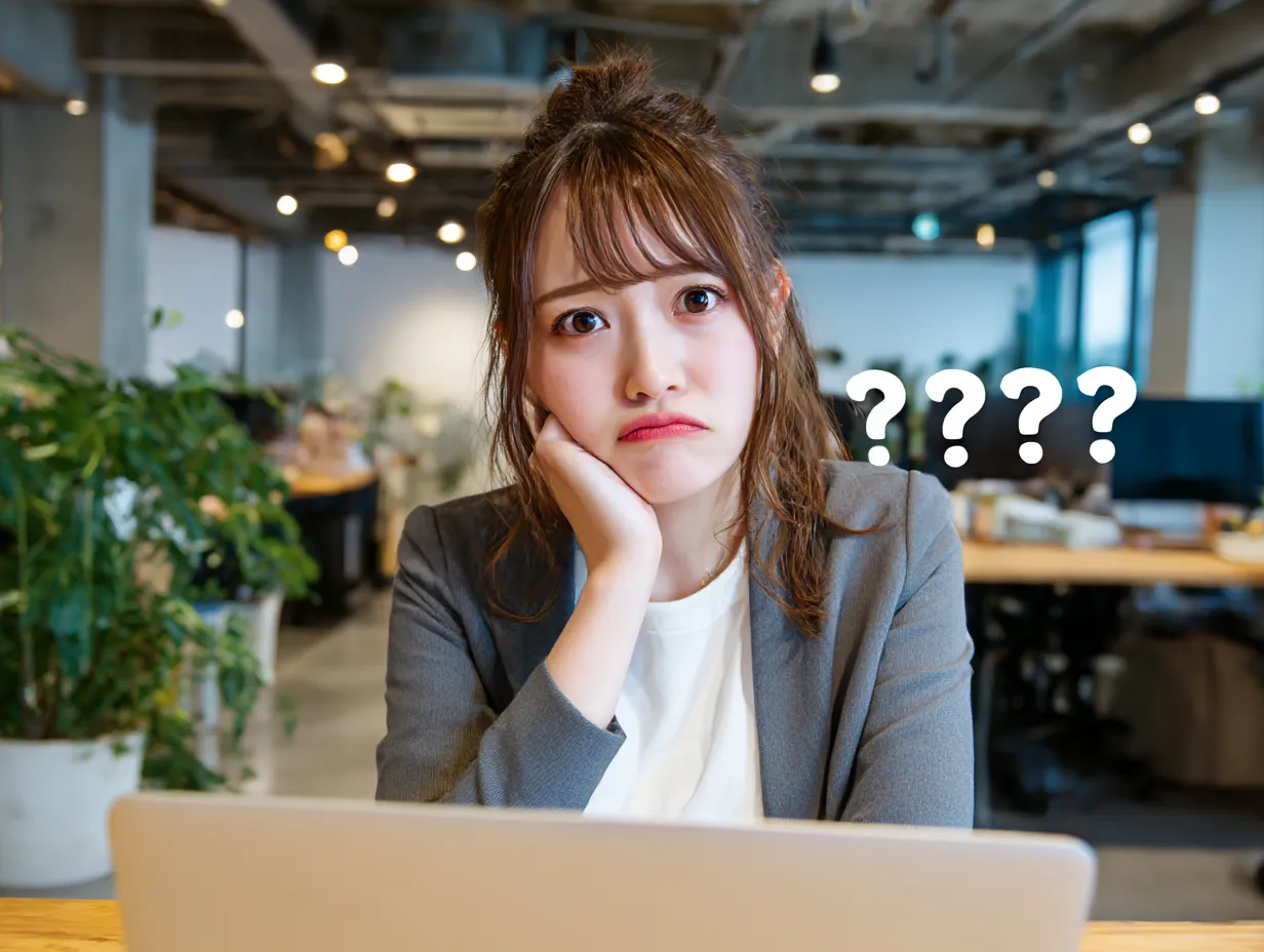 はてな顔の女性とパソコン｜疑問を抱えた女性がノートパソコン前で頬杖をつくポーズ。背景のオフィス空間と「？？？マーク」が加わり、はてなを感じる場面の演出に最適なビジネス向け写真です。
