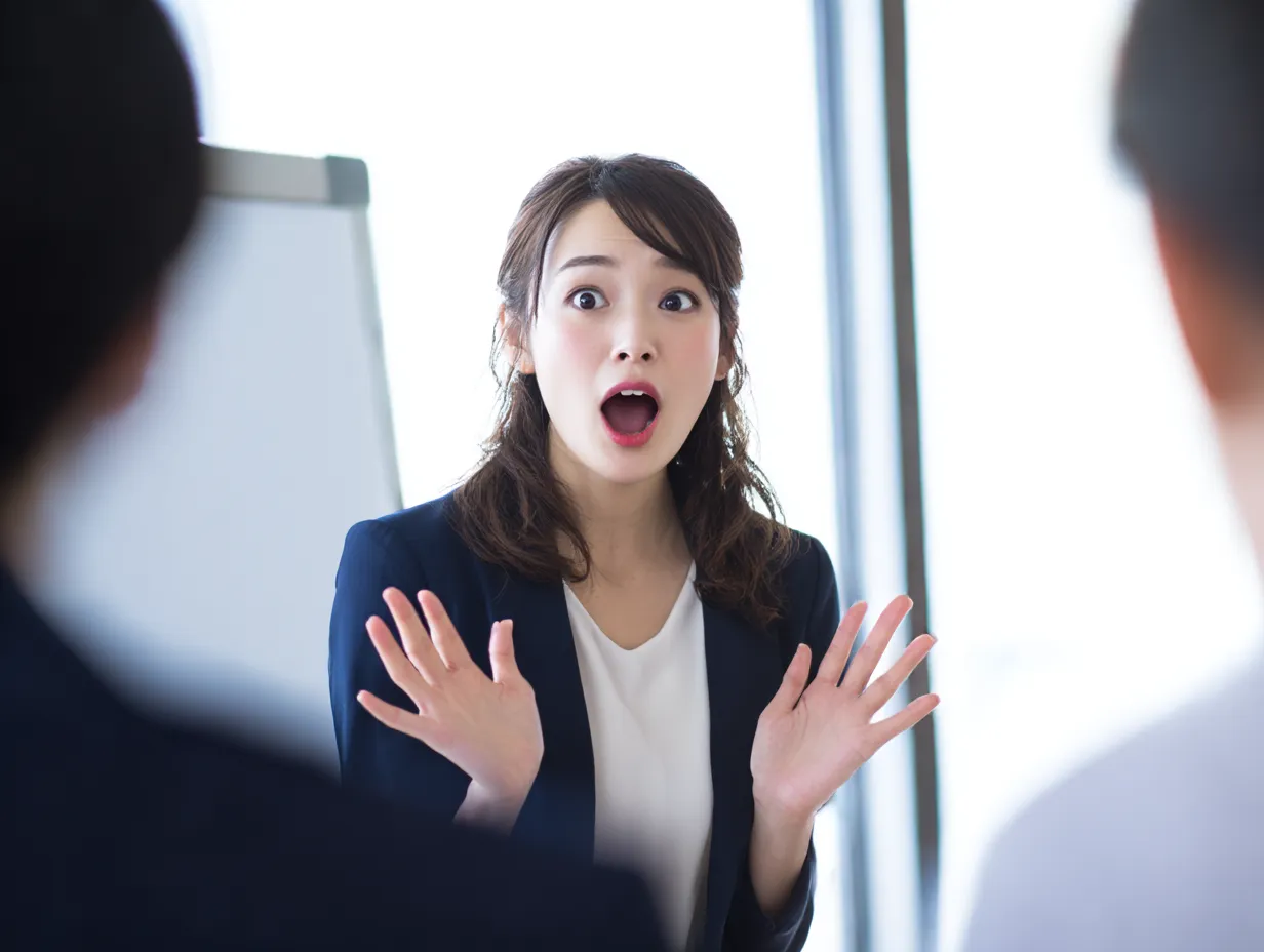 驚きを見せる女性プレゼンター｜プレゼン中の女性が、手を大きく広げて驚きを表現する場面。背景の会議室と登場人物の対比が、シーンに緊張感と軽やかさを添えた実用的なビジネス素材です。