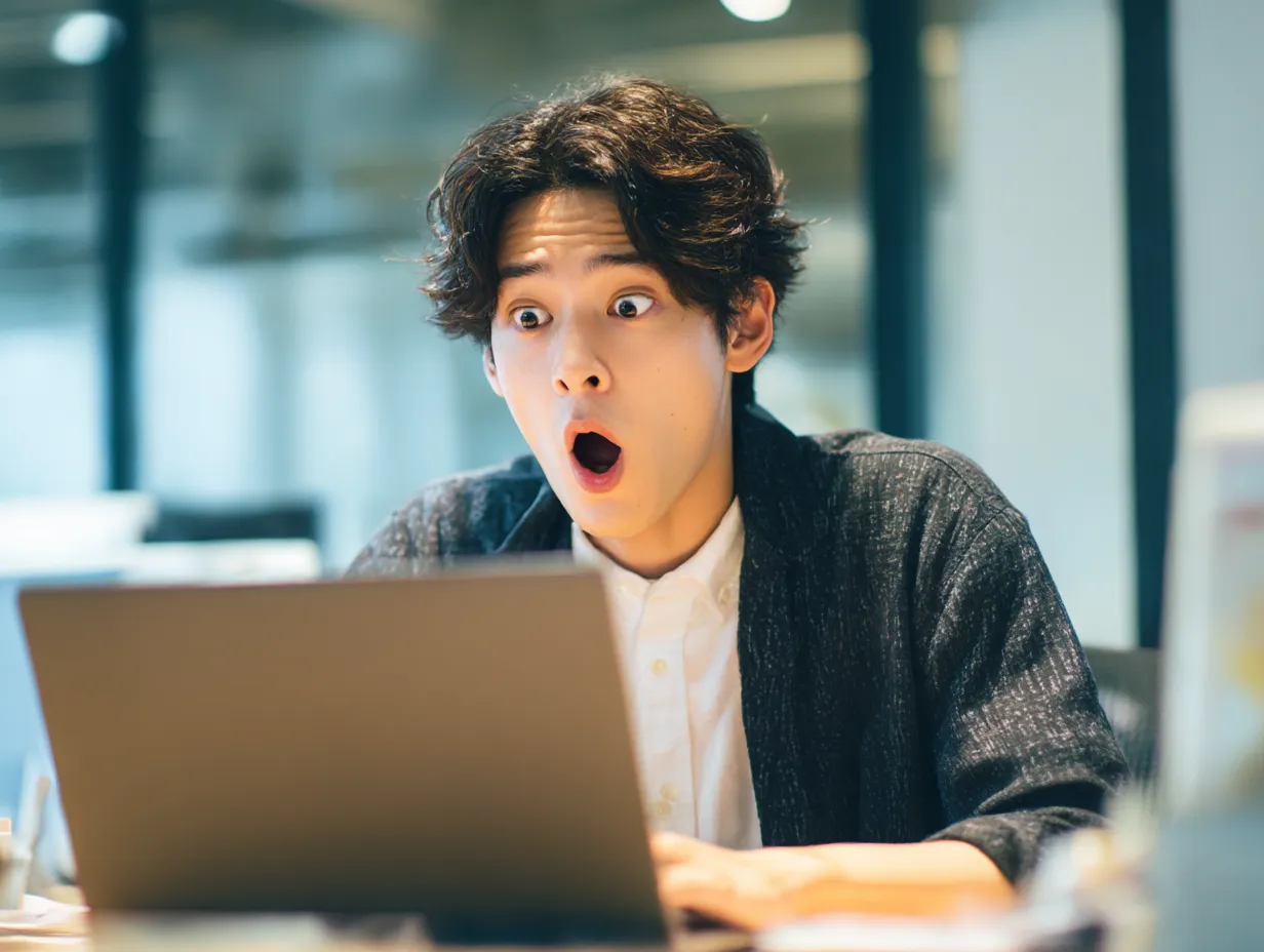 びっくりした視線の若手ビジネスマン｜画面に釘付けになった様子のびっくり顔が目を引く構図。明るく清潔感のある空間で、SNSや情報の拡散、想定外の事態を知らせるイメージに最適な素材です。