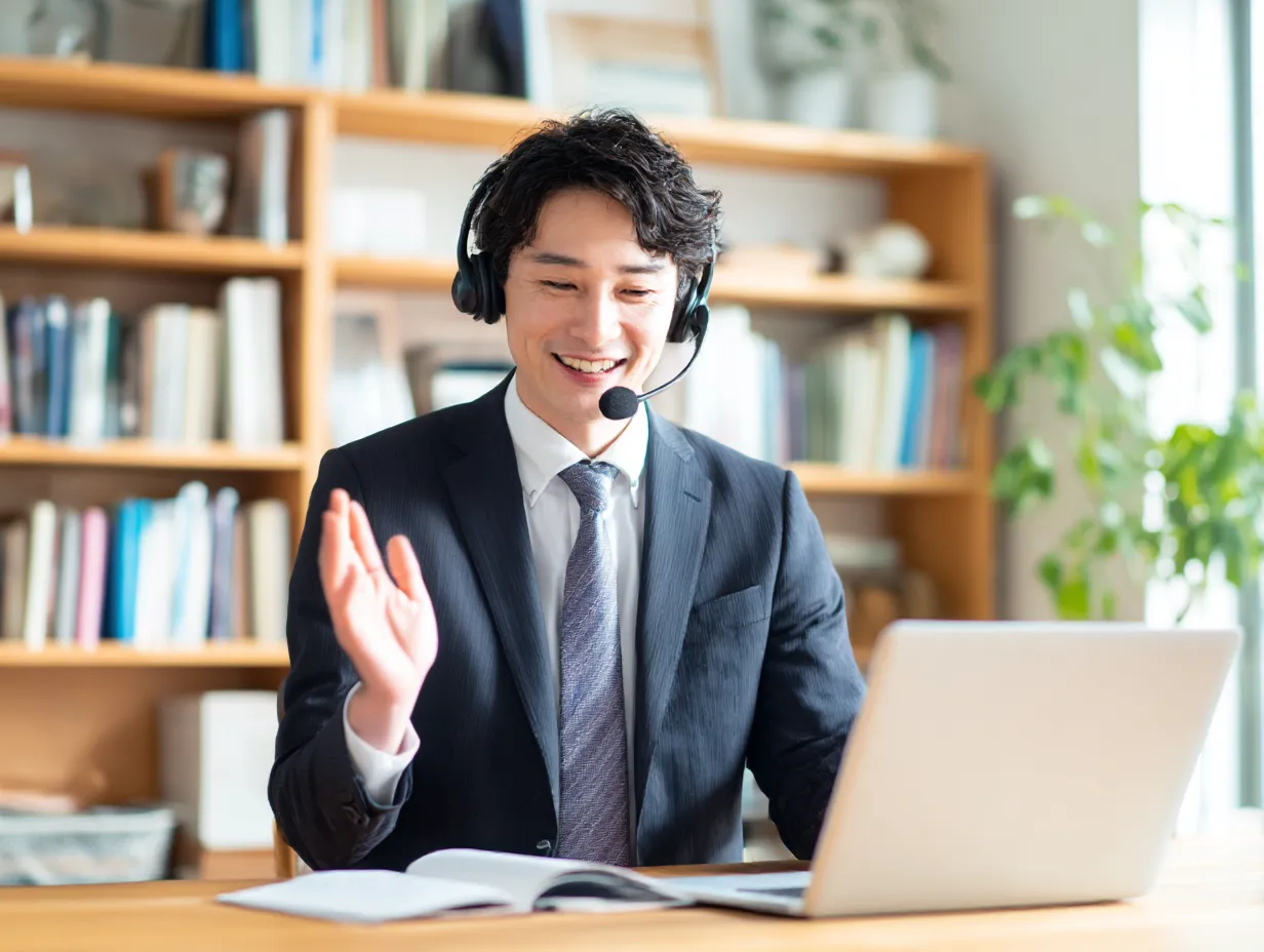 オンラインで案内する男性の案内｜ヘッドセットを装着し笑顔で話すスーツ姿の男性。リモート対応での丁寧な「案内」を表現しており、信頼感と親しみやすさを演出するビジネスシーン。