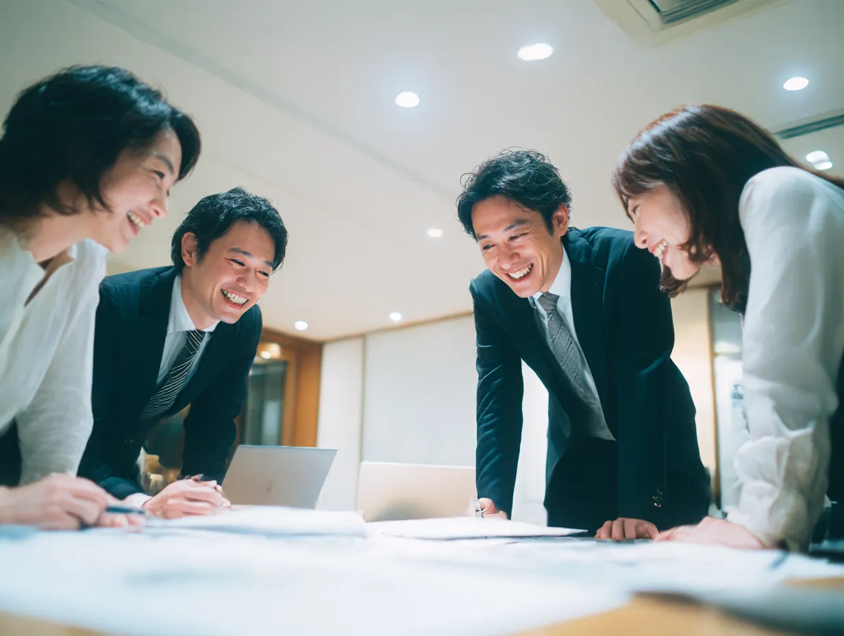 笑顔でアイデアを出し合うチームの話し合い｜机に身を乗り出して笑顔で意見を交わすビジネスパーソンたち。前向きで活発な「話し合い」の雰囲気を捉えた、チームワークの良さが伝わる素材。