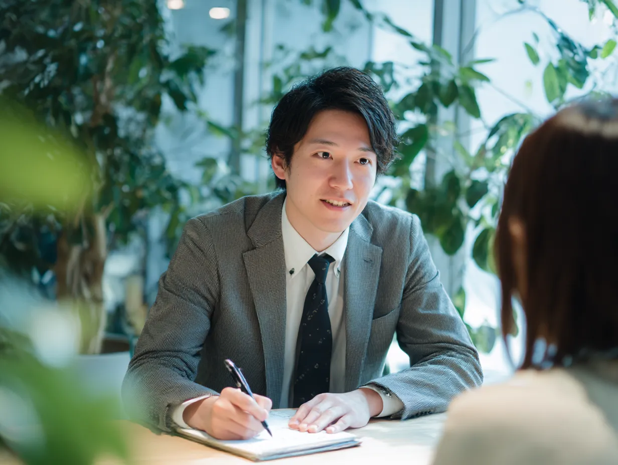 聞く力を持つ若手社員の面談｜落ち着いたスーツ姿の社員が真剣に相手の話に耳を傾ける様子が描かれており、「聞く」姿勢が信頼感を生むという印象を与えるオフィス素材に適した構成。