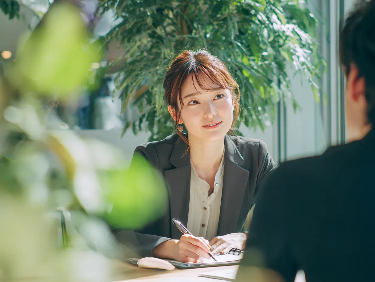 聞く力を持つ若手女性社員｜明るく開放的な空間で、相手の話に耳を傾けるビジネスウーマンの表情が魅力的。「聞く」姿勢から信頼関係や共感の雰囲気を表現している。