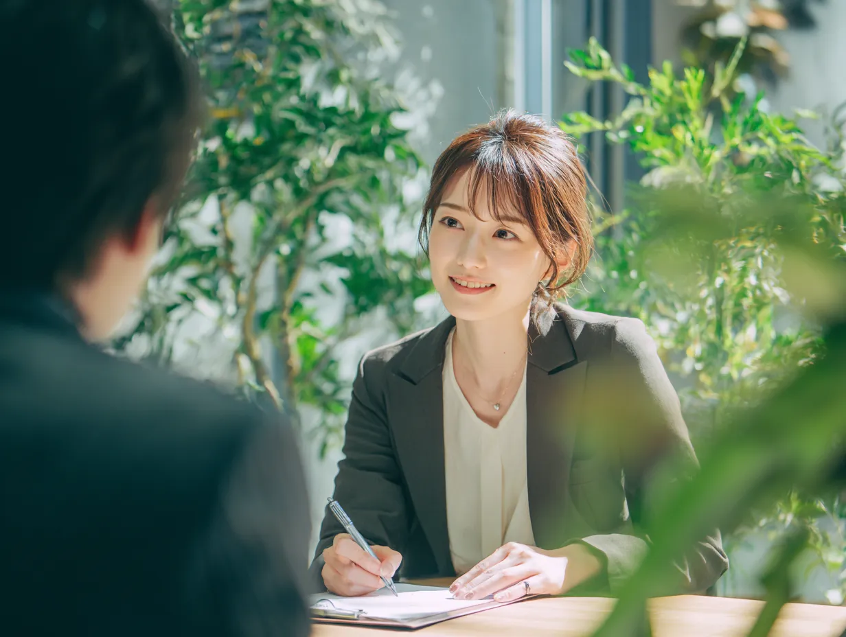 聞く姿勢で対話する女性社員｜ナチュラルなグリーン背景の中、相手とアイコンタクトを取りながら「聞く」女性社員の姿が印象的で、やわらかい対話のイメージを醸成。