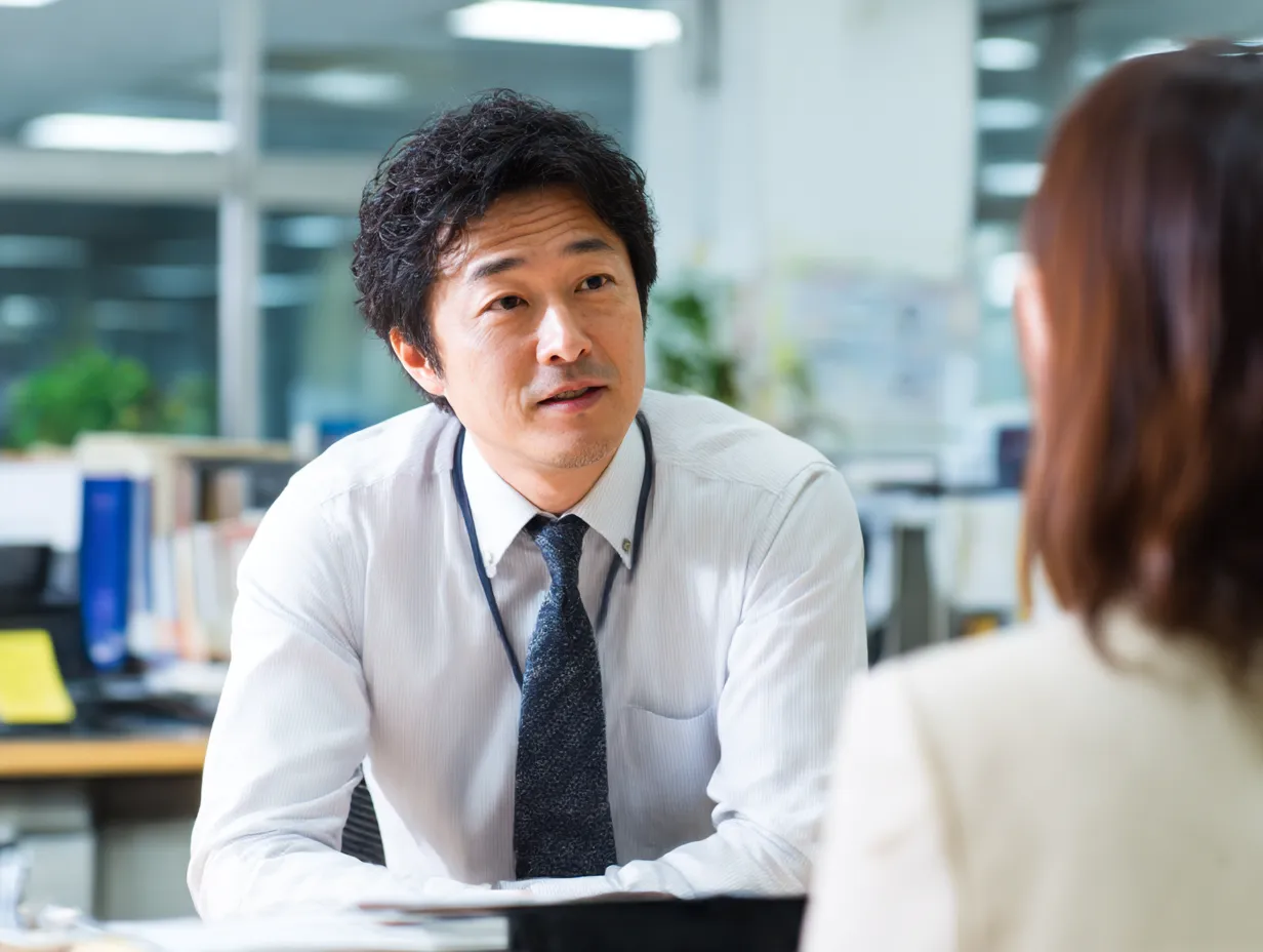 相談を聞く中堅ビジネスマン｜オフィス内で真剣に話を「聞く」中堅社員の姿が印象的。柔らかな表情が信頼感を醸し、日常の業務相談シーンとして汎用性の高いビジネス素材。