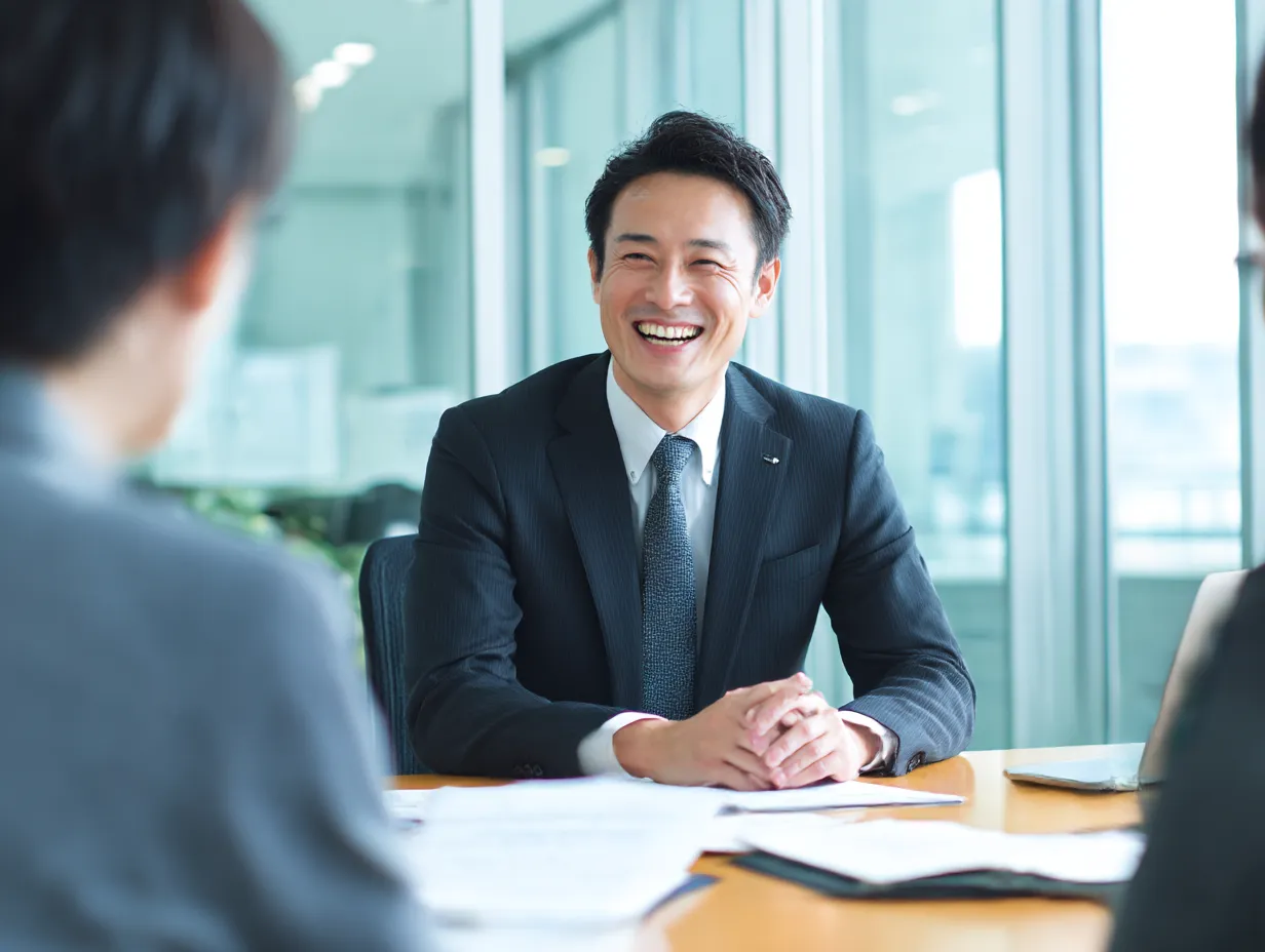 相談に耳を傾ける男性上司の表情｜明るいオフィス空間で、部下の話に真摯に「聞く」姿勢を見せる男性上司。フラットで開かれた組織文化を伝える写真として活用できる。