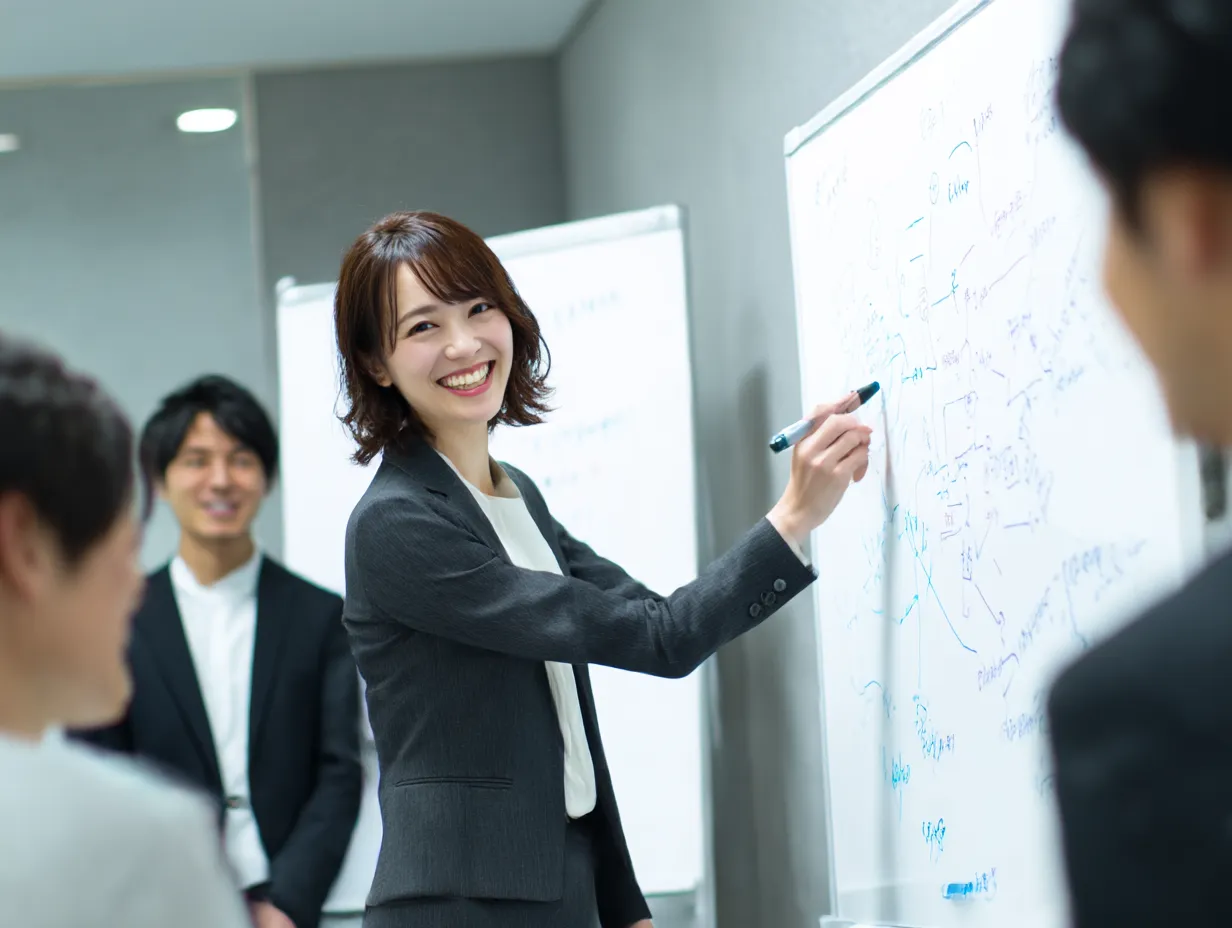 笑顔で聞く女性プレゼンター｜ホワイトボードの前で話しながらも聴衆の反応を楽しそうに「聞く」姿が魅力。前向きで活発な議論を象徴するシーンにふさわしい構成。