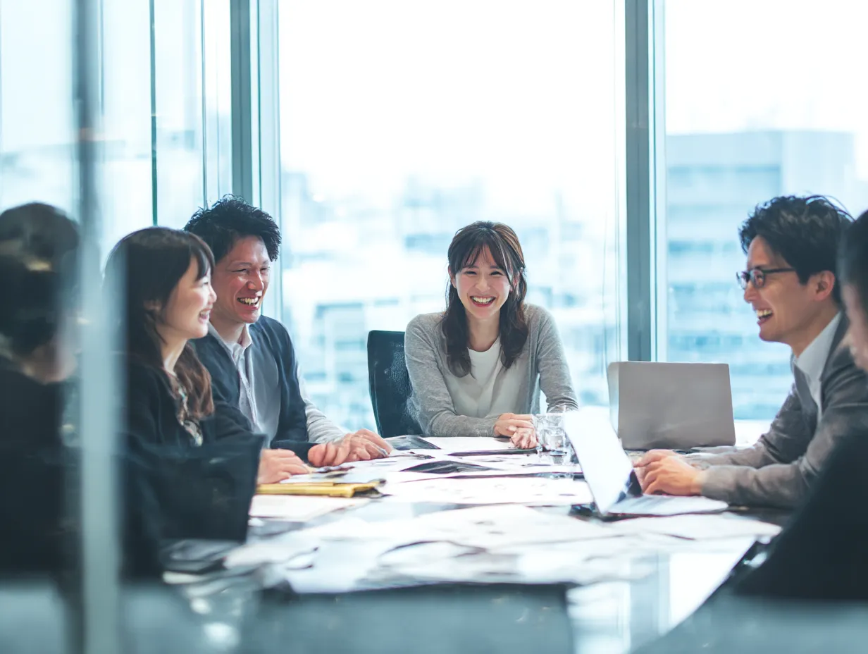 和やかな会議で聞くチームの輪｜都市型オフィスで、笑顔のメンバー同士が互いの意見を「聞く」温かい雰囲気を捉えた一枚。フラットな関係性や風通しの良さを伝える素材。