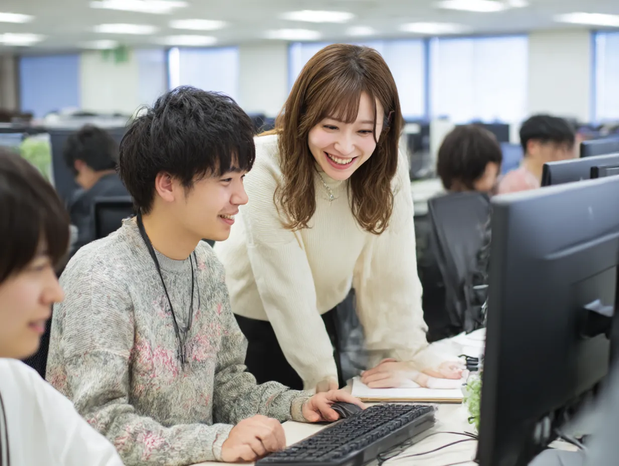 研修中のオフィス内サポート風景｜PCに向かいながらペアで作業する若手社員たち。明るいオフィス空間での「研修」やOJT場面に最適で、協働や学び合いの雰囲気を自然に映し出している。