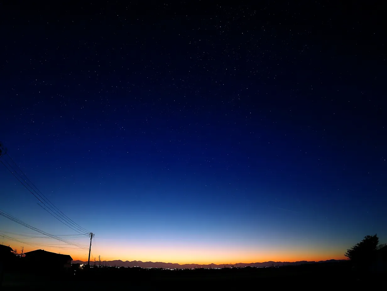 エモい空と夜明けの街並み｜地平線からの光と深い青の夜空が美しいグラデーションを描き出すエモい空の写真です。街灯と山影がシルエットとして浮かび上がり、静けさと希望を同時に表現しています。背景素材に最適です。