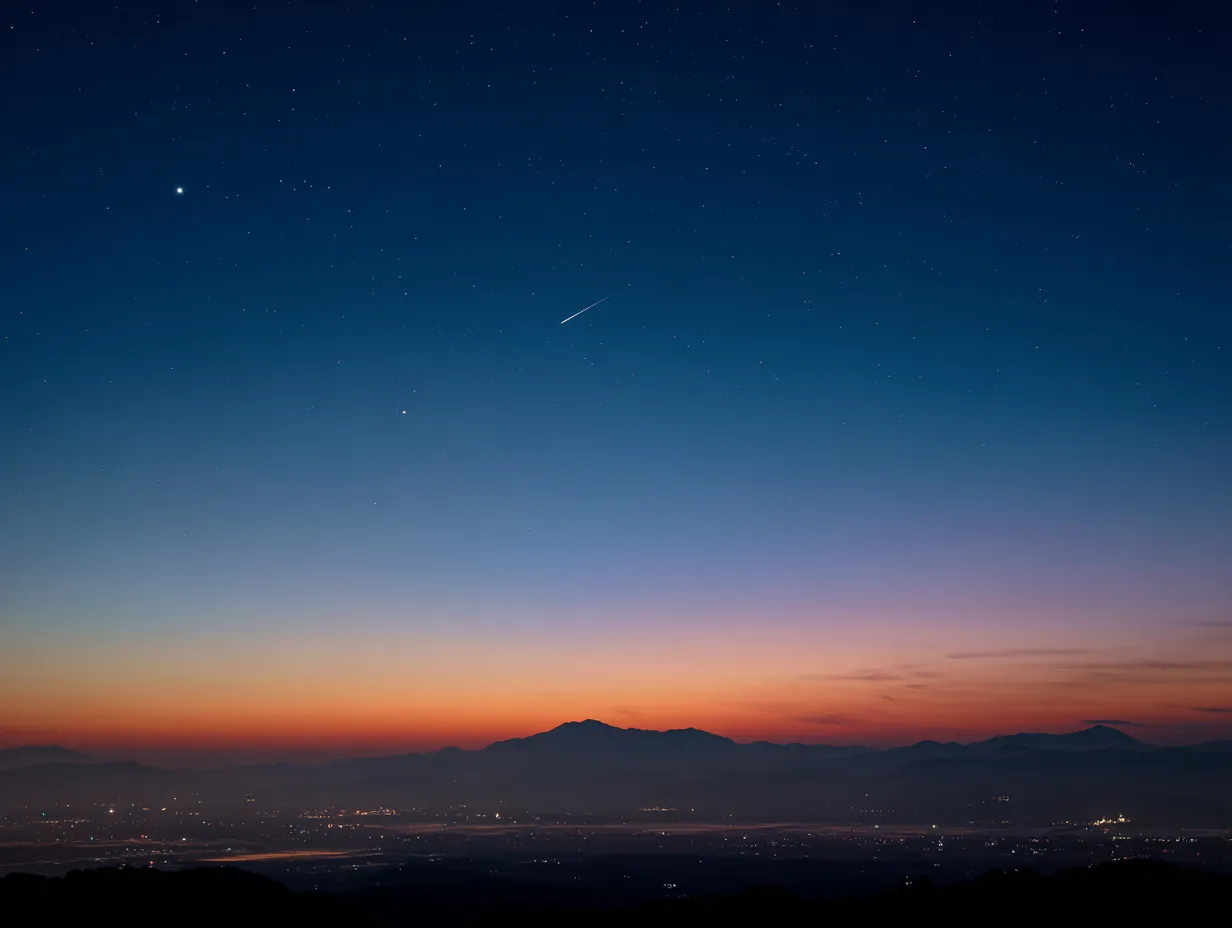 エモい空と流れ星の風景｜夜明け前の都市と山並みに、流れ星が一筋走るエモい空のシーンです。オレンジから群青への色彩変化がドラマチックで、未来や夢を想起させます。プレゼン資料や記事のビジュアルに活用できます。