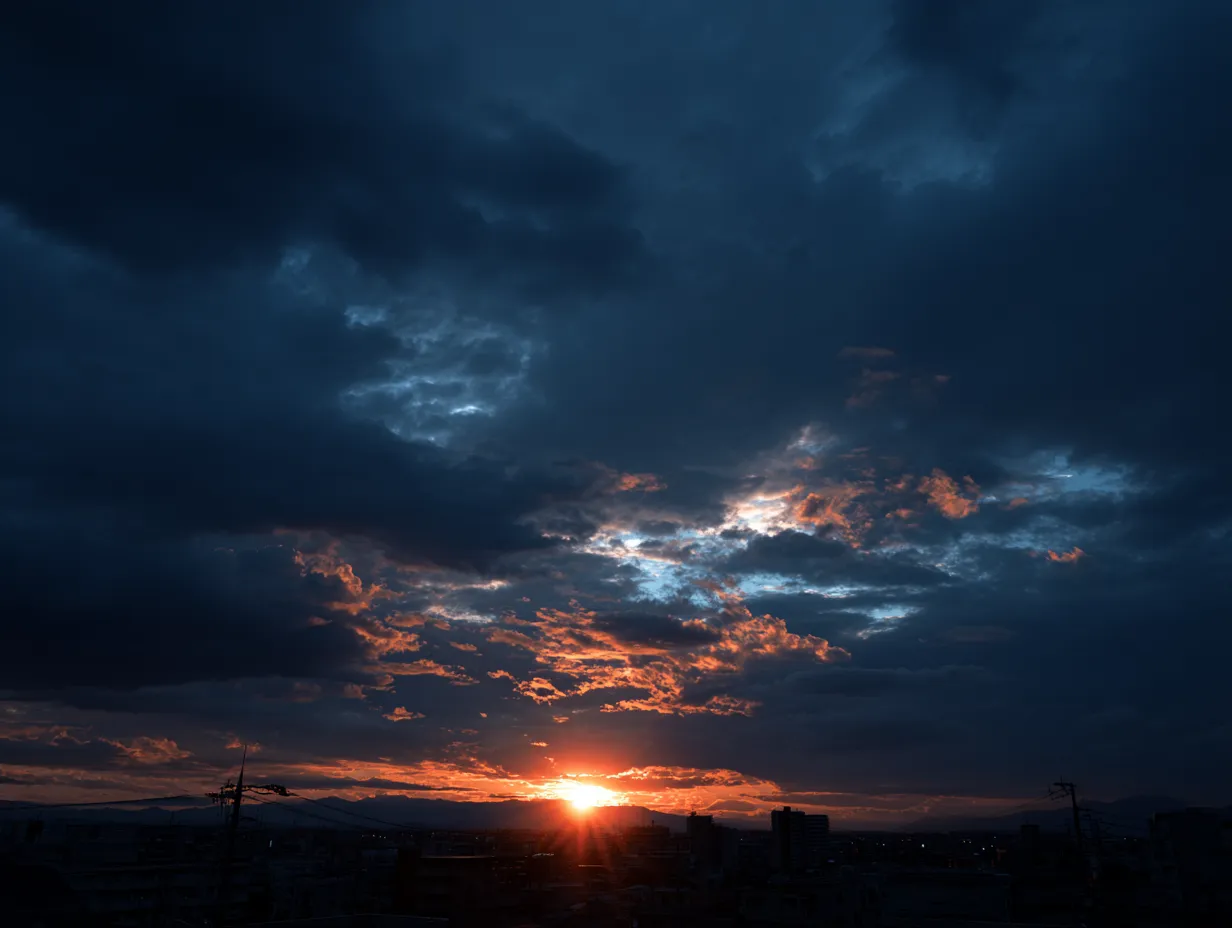 エモい空と沈む夕日｜厚い雲の隙間から夕日が沈む瞬間を切り取ったエモい空の写真です。青と赤のコントラストが重厚で、落ち着きや余韻を表現するのに最適な素材です。記事や広告に活用可能です。
