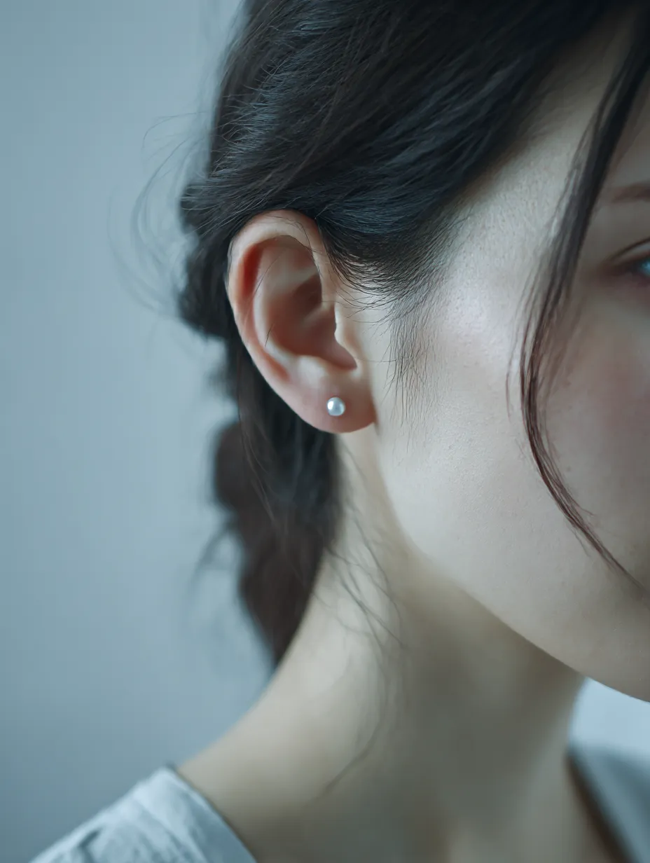 耳に光る粒｜女性の耳に小さな真珠のピアスが輝き、透明感ある肌と共鳴するように映し出されている。柔らかな光が耳の輪郭を際立たせ、髪の影が静けさを添える構図となっている。