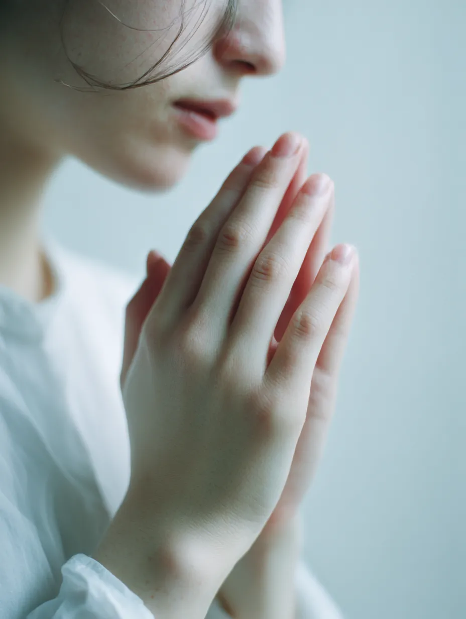 願いを秘めて手を合わせる｜頬にかかる髪と淡い表情が、手を合わせる仕草に寄り添う。近接した視点が細やかな肌の質感を強調し、人物の内なる思いを際立たせている。