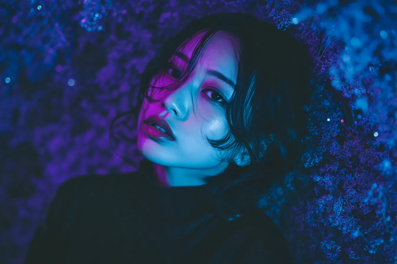 紺色背景とネオンに染まる女性｜艶やかな光が顔を照らす中、紺色背景に浮かび上がる女性の表情がドラマティックで、都会的な感性を刺激する構成の背景素材です。