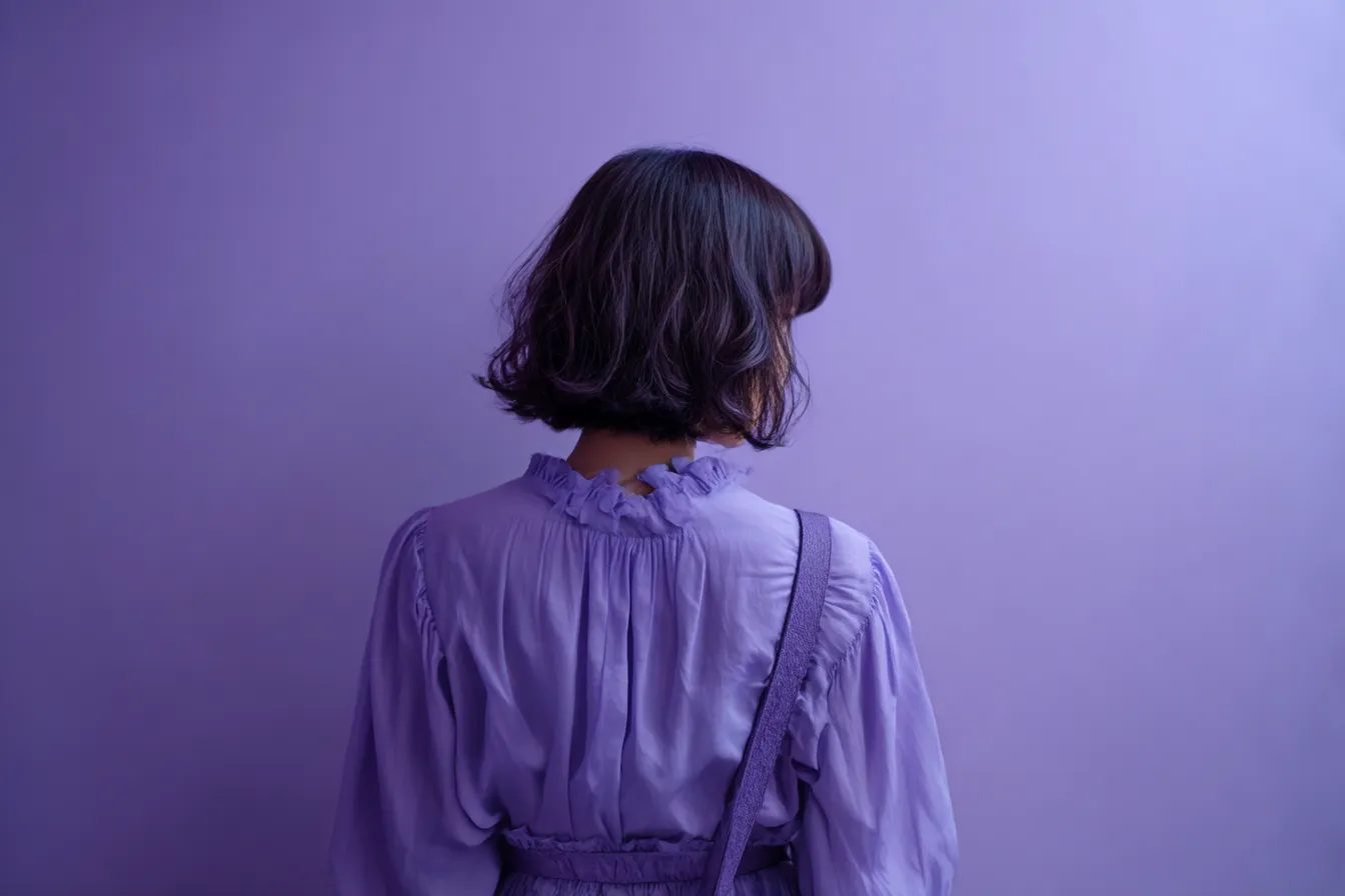 紫背景と後ろ姿の少女｜シンプルな構図により背中越しの人物像が際立ち、ラベンダー寄りの紫背景が柔らかでミニマルな雰囲気を醸します。