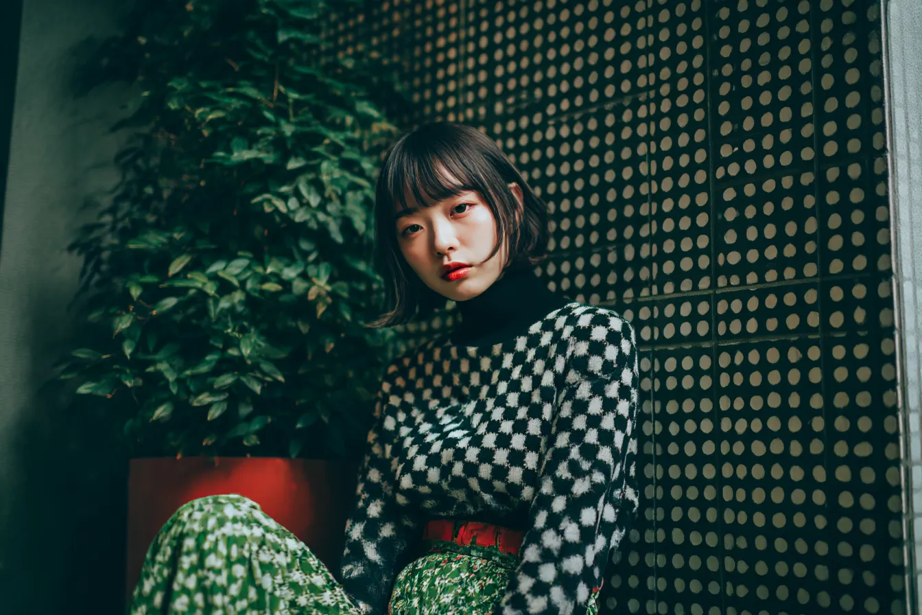 ドット背景とグリーンパンツの少女｜壁面の整然としたドット模様とファッションの組み合わせがユニークで、日常感と構成美が調和した背景です。