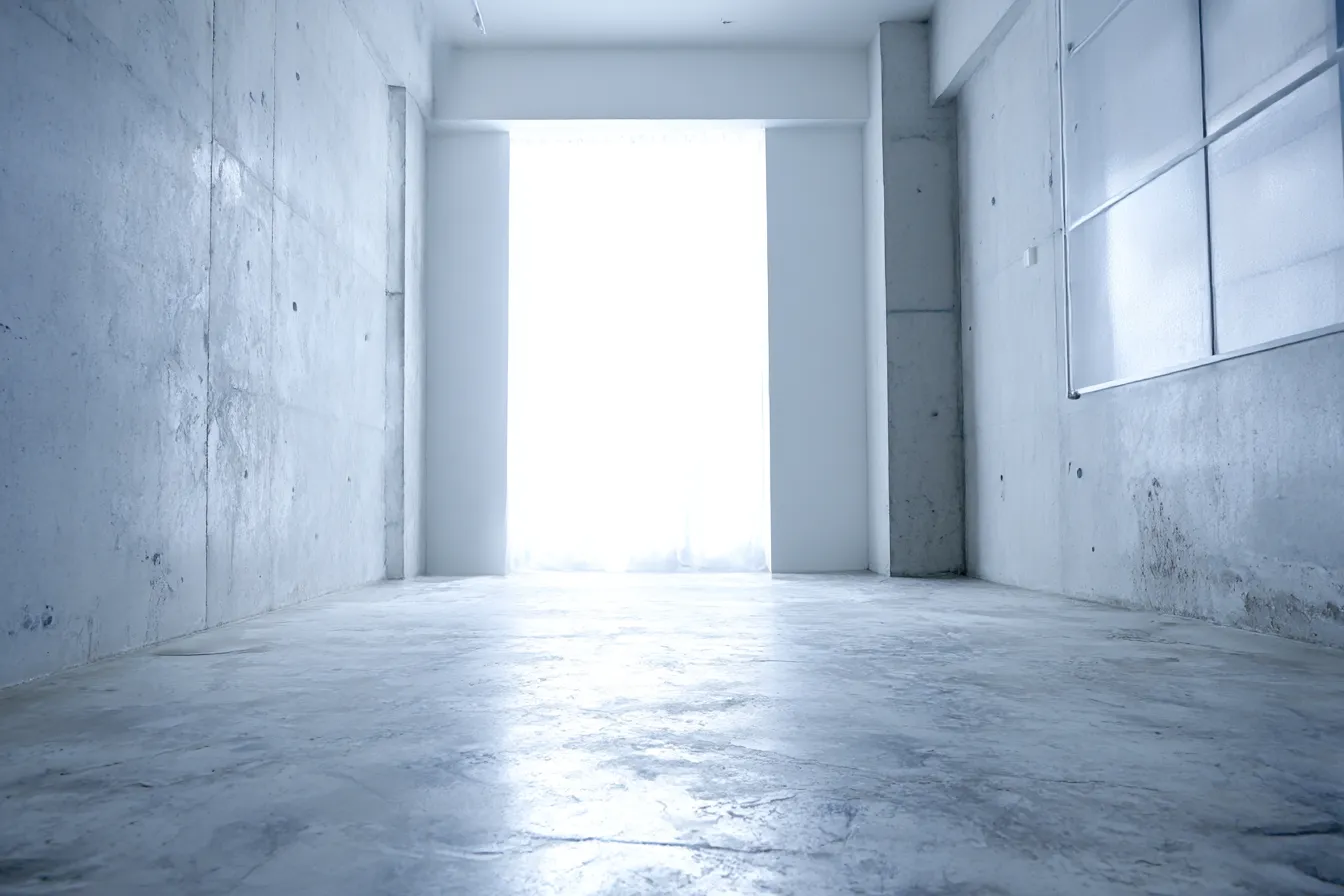 白背景の無機質コンクリート空間｜荒れた床面と打ちっぱなしの壁が、白背景の強い光に包まれ対照を成す。素材のリアリティを際立たせた静かなインダストリアル演出。