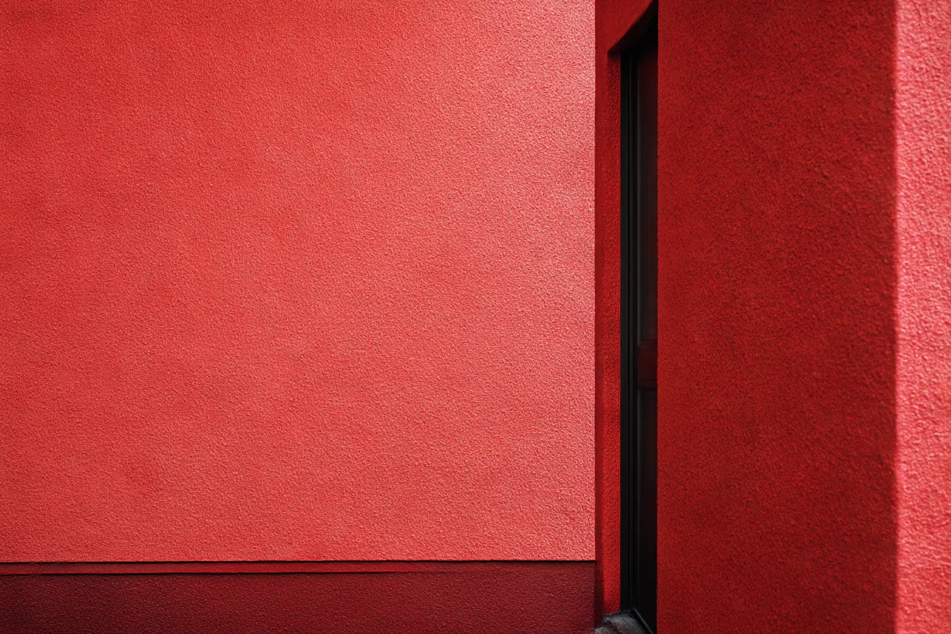 赤背景の角張った壁面配置｜二面の外壁が構成する建築の角が主題。赤背景が建築素材の表情を際立たせ、視覚的リズムと硬質な存在感を際立たせている。