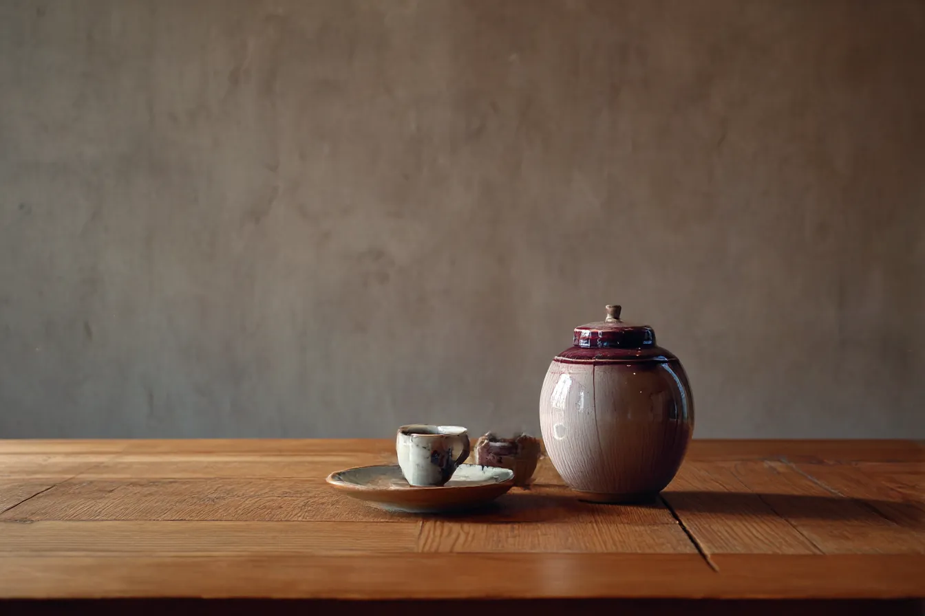 茶器と木のテーブルの茶色背景｜素焼きの器と木製のテーブルが無機質な茶色背景の中で調和し、落ち着いた温かみを演出する構成でミニマルな静寂を感じさせます。