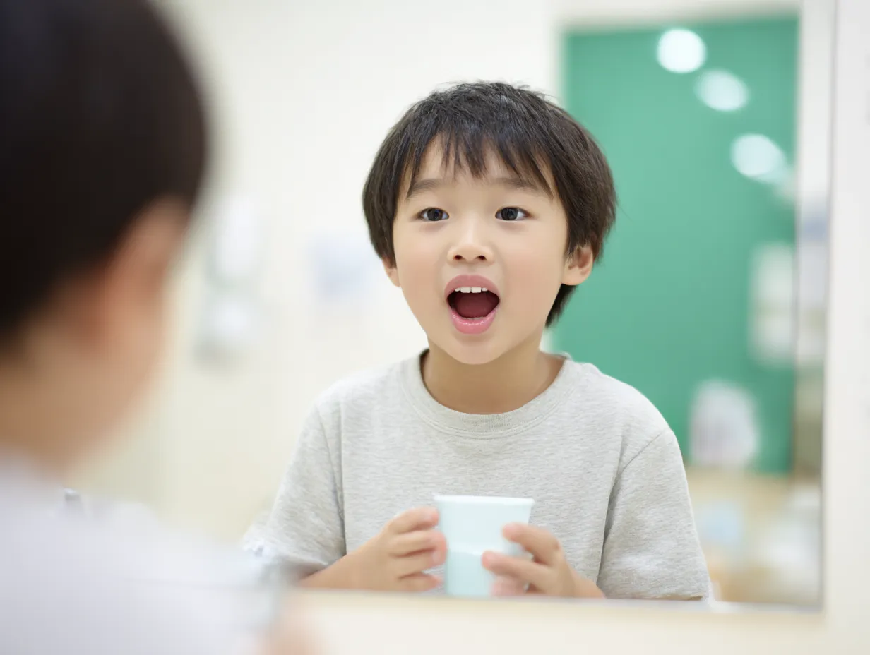 小学生男児のうがい写真（学校）｜明るい室内で鏡越しに口を開けてうがいする小学生の男の子。教育施設らしい背景と自然な表情が、集団生活での衛生習慣の大切さをやさしく伝える。