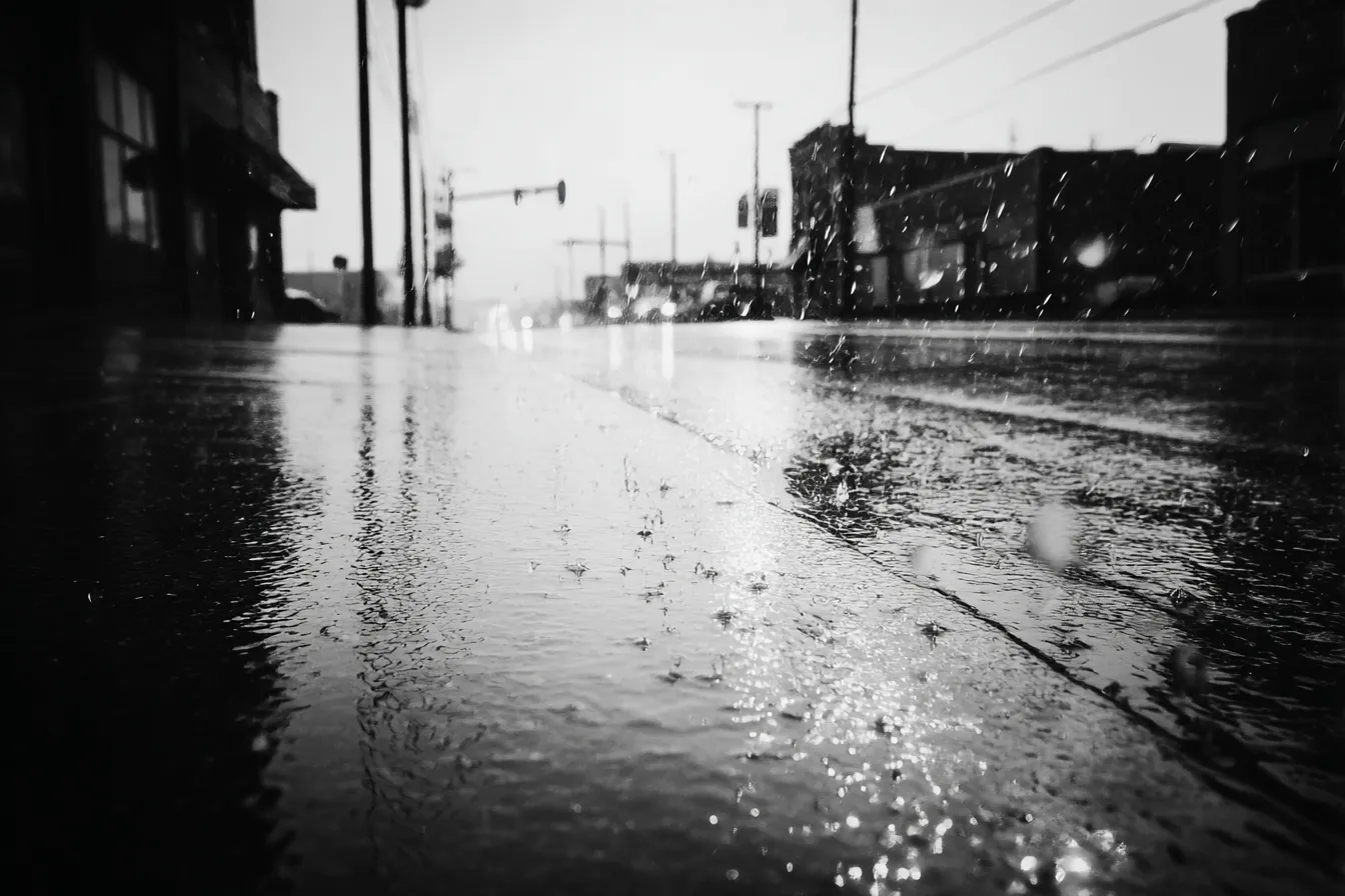 白黒背景に濡れた街路の雨｜濡れた道路に反射する光と雨粒が動きを生む都市風景。ハイコントラストな白黒背景がノスタルジックかつ力強い空気感を伝えている。