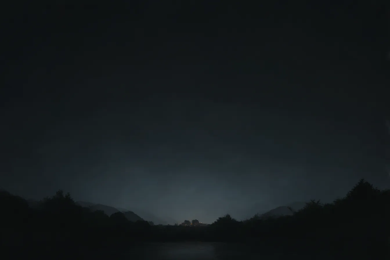 黒の背景に灯る遠景の集落｜漆黒の空と山に囲まれた中、遠くの集落だけが柔らかい光で浮かび上がる構図。黒の背景が夜の静寂と孤立感を引き立てる。