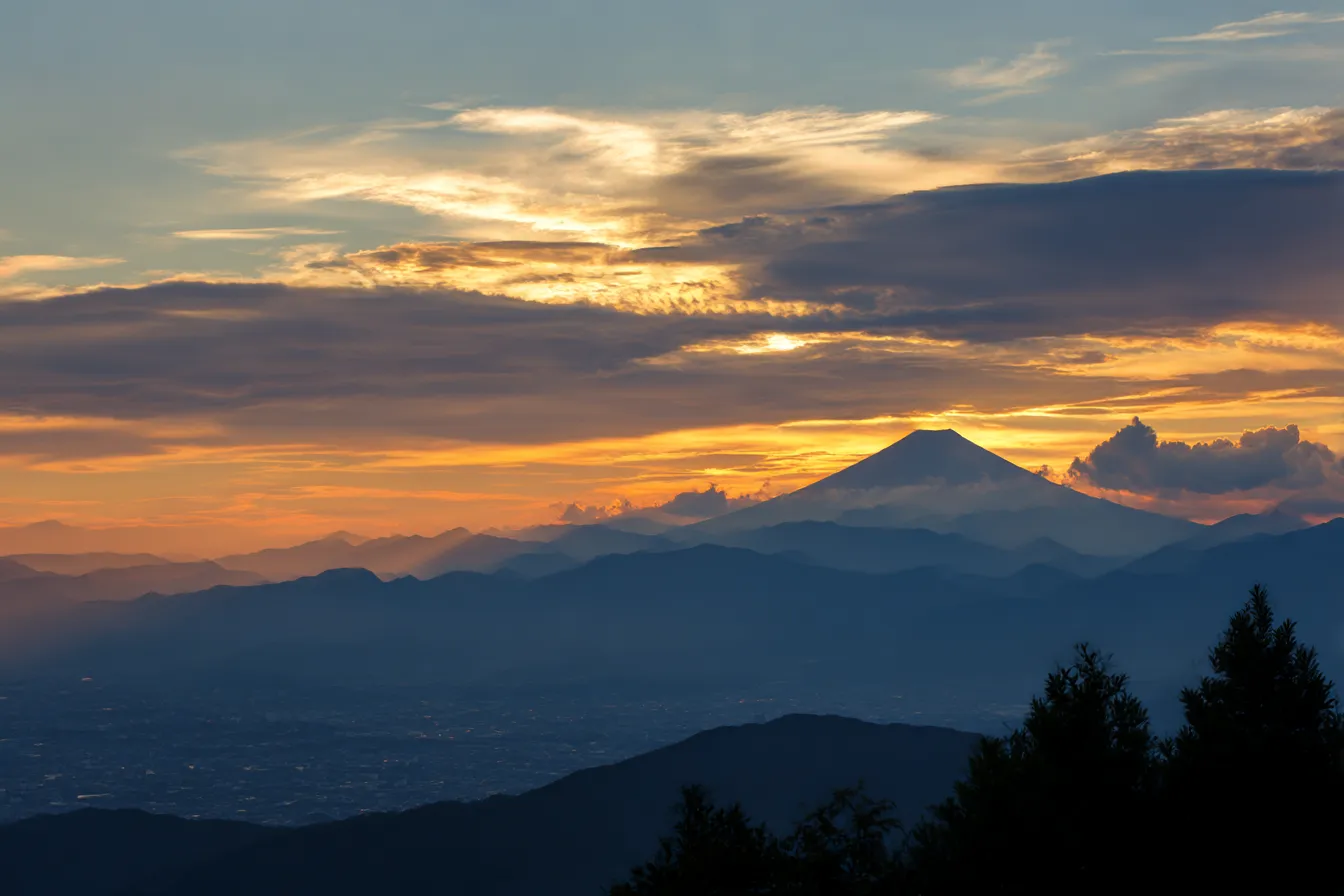 秋の雲・写真に映る富士山と夕焼け雲｜夕焼けに染まる空を背景に、富士山がシルエットとなって浮かび上がる。層状の雲とやわらかな光のグラデーションが、ドラマティックで荘厳な秋の余韻を描く。