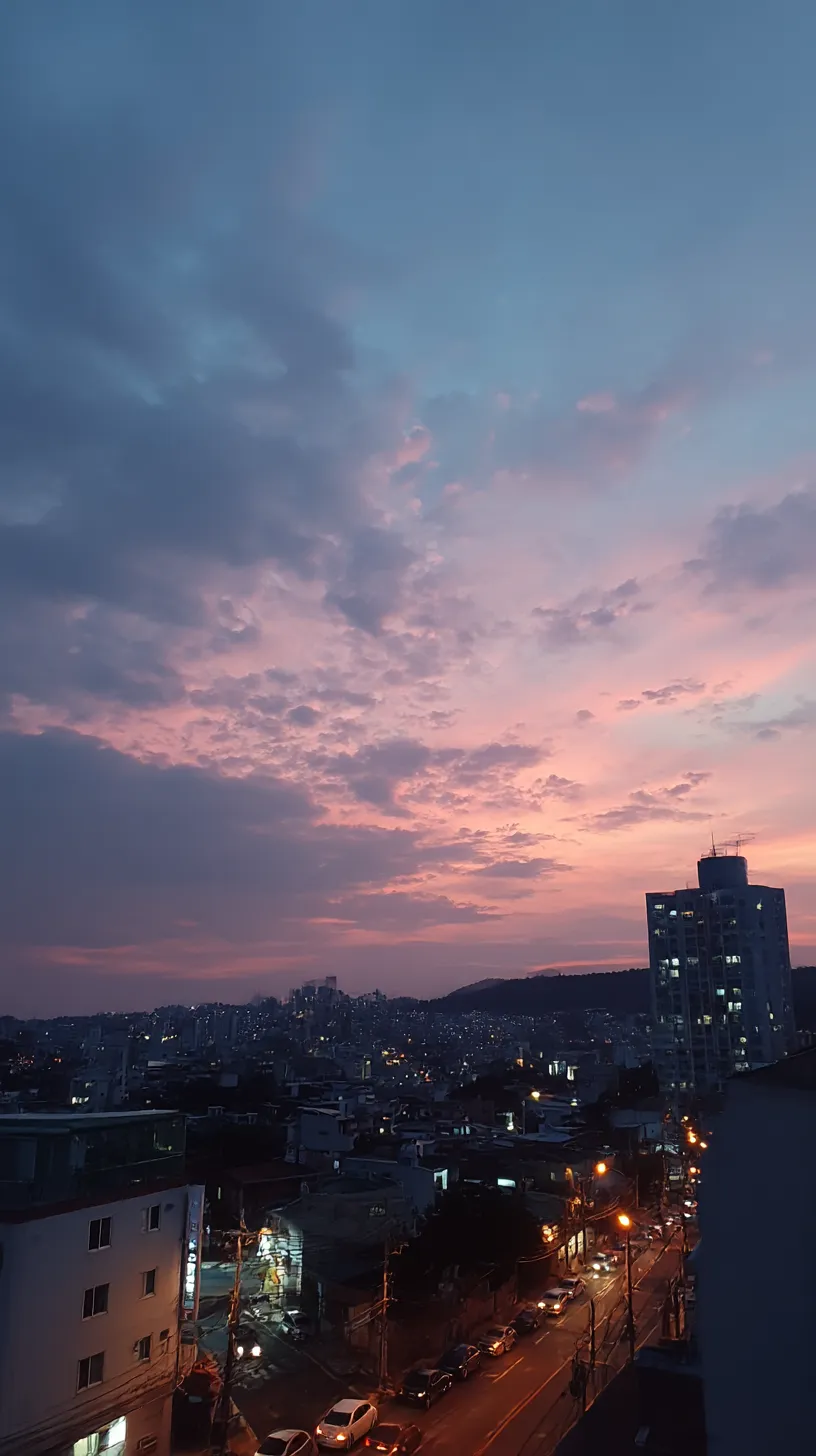 エモい韓国壁紙 夕暮れの街灯｜ピンクと群青が交差する夕焼け空の下、街灯のオレンジが灯り始める情景が広がるエモい韓国壁紙。暮れゆく空と都市の光が切なさを漂わせる構図。