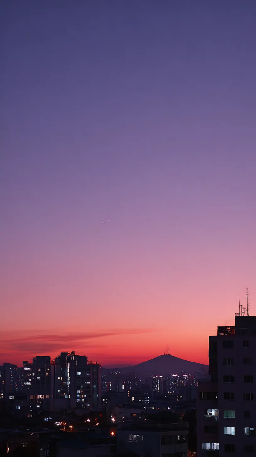 紫エモい韓国壁紙 黄昏の街｜ビル群と山影の向こうに沈む夕日が紫から赤へと溶け込み、夜の訪れを告げる。紫エモい韓国壁紙らしい鮮やかな空色が幻想的な印象を深める。