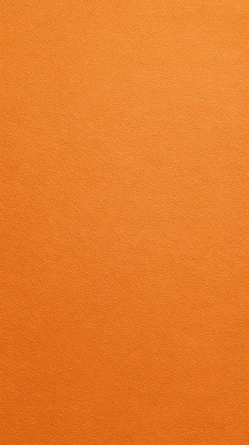 オレンジの無地壁紙 微細な粒子感｜画面全体に細やかな粒子が散りばめられたような表情を持ち、オレンジの明るさに深みを与える。均一でありながらも動きを秘めた質感が、静けさと親しみを同時に感じさせている。
