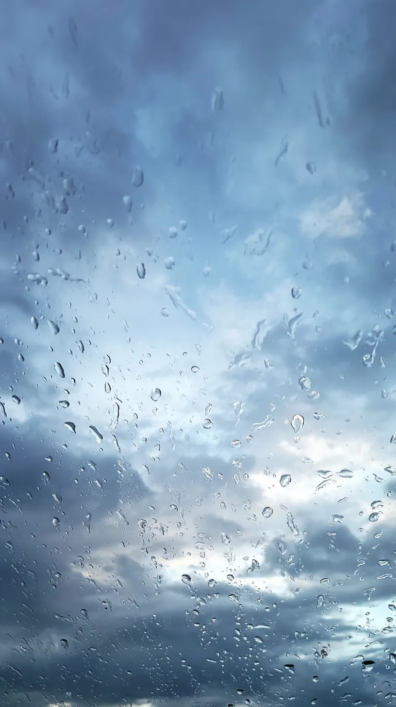エモい空 壁紙 雨粒の窓越し｜窓ガラスに散る雨粒と曇り空が重なり、揺らめく水滴が幻想的な模様を描くエモい空の壁紙。静かな時間の中で感情を映し出すような透明感が広がる。