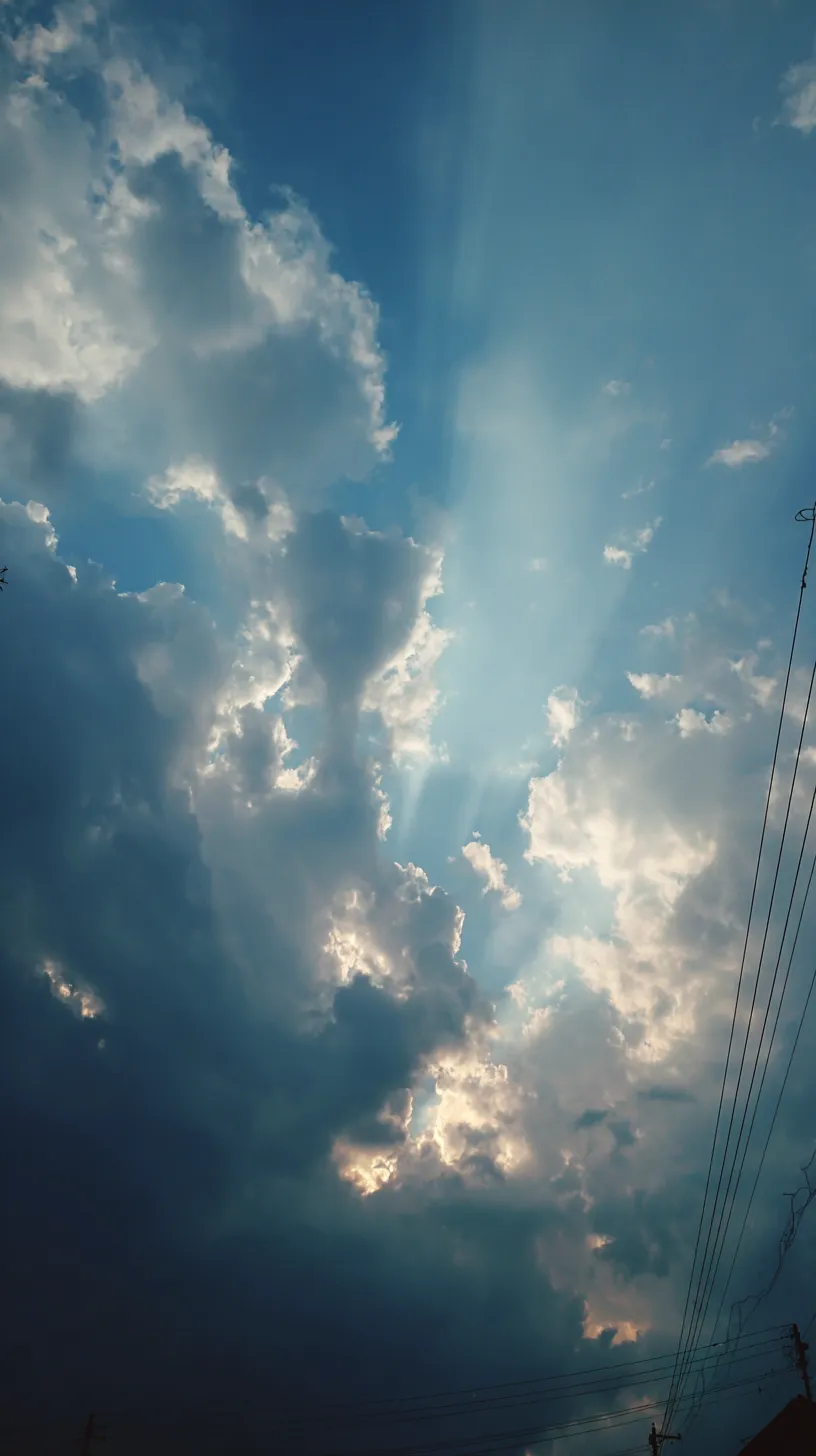 エモい空 壁紙 光の雲間｜分厚い雲の隙間から差し込む光がドラマチックな印象を与えるエモい空の壁紙。青空と闇雲のコントラストが心を揺さぶる強い表情を持っている。