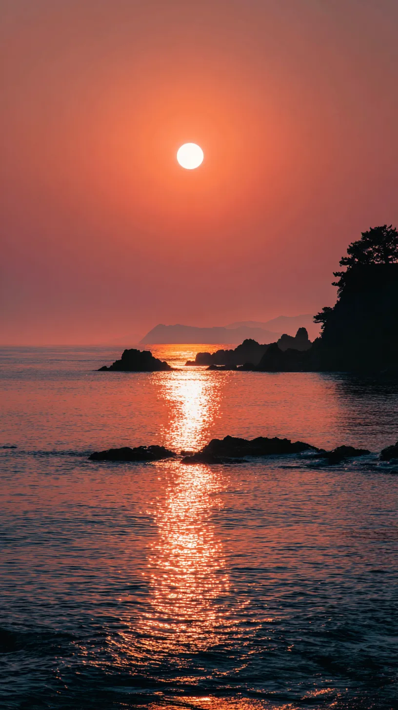 夕暮れ太陽の壁紙｜水平線に沈む太陽が赤く輝き、シルエットの岬と穏やかな海が重なる太陽の壁紙。幻想的な余韻を漂わせる温かな景色。