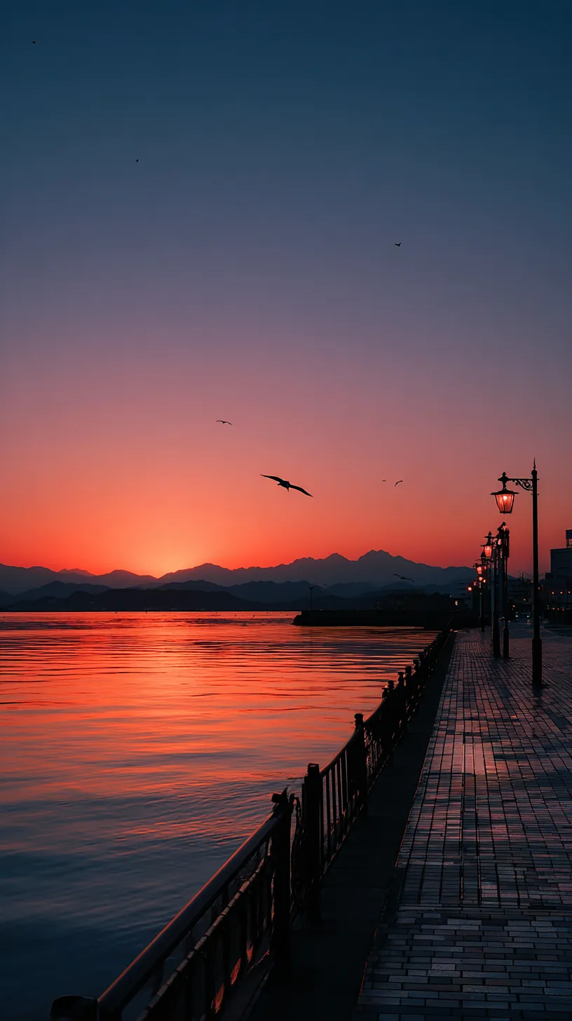 夕焼け壁紙の海辺｜深い群青と赤橙が溶け合う夕焼け壁紙。海面に光が反射し、飛ぶ鳥の姿が加わることで、静謐な時間の流れを感じさせる美しい表現。